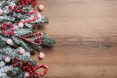 Beautiful Christmas tree branches with decorative berries, candy canes and ornaments on wooden background, flat lay. Space for textの写真素材