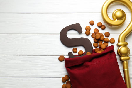 Sinterklaas (Saint Nicholas) Day. Sack with kruidnoten cookies, chocolate letter S and crosier on white wooden background, flat lay. Space for textの写真素材