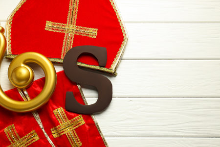 Sinterklaas (Saint Nicholas) Day. Chocolate letter S, mitre, stole and crosier on white wooden background, flat lay. Space for textの写真素材