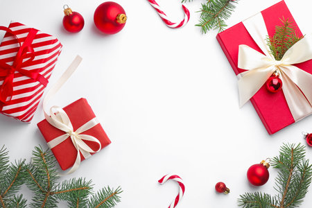 Frame made of fir tree branches, gift boxes and Christmas decor on white background, flat lay. Space for textの写真素材