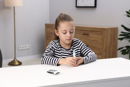 Diabetes. Little girl checking blood sugar level with lancet pen at white table indoorsの写真素材