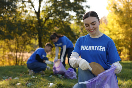 Group of happy volunteers with bags collecting trash in park, selective focusの写真素材