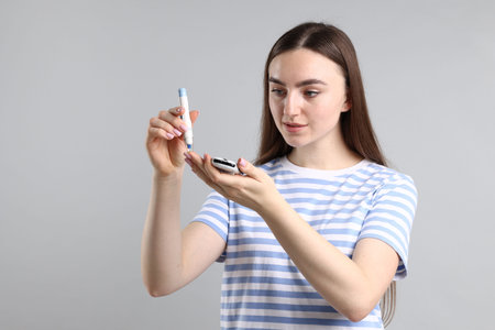 Diabetes. Woman checking blood sugar level with lancet pen and glucometer on gray background