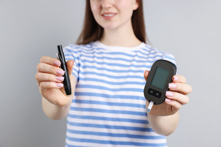Diabetes. Smiling woman with lancet pen and glucometer on gray background, closeupの写真素材