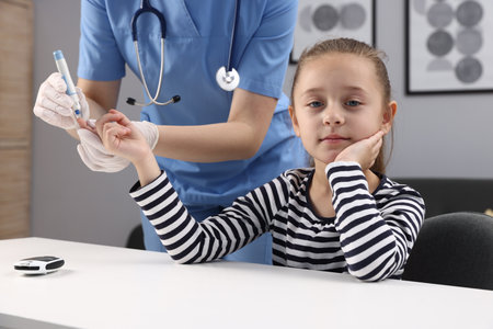 Diabetes. Doctor in medical gloves checking little girl's blood sugar level with lancet pen at white table indoors, closeupの写真素材