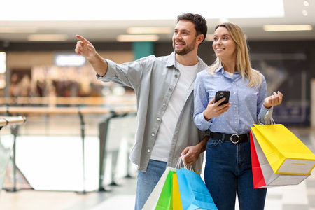Happy couple with shopping bags and smartphone walking in mallの写真素材