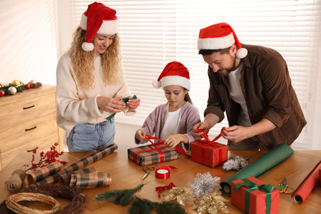 Happy family in Santa hats wrapping Christmas gifts at table indoorsの写真素材