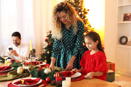 Little girl setting table with her mom in room decorated for Christmasの写真素材