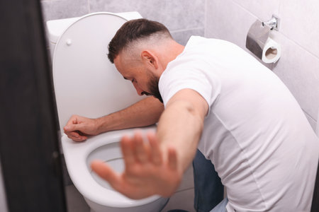 Man suffering from nausea over toilet bowl in bathroomの写真素材
