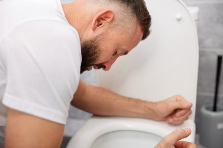 Man suffering from nausea over toilet bowl in bathroomの写真素材