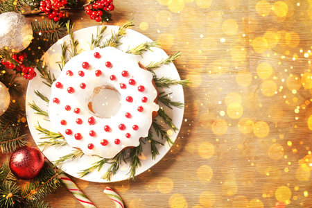 Tasty Christmas cake with red currants, fir branches and festive balls on wooden table, flat lay. Bokeh lightsの写真素材