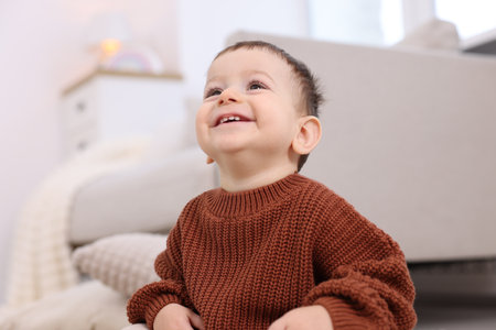 Cute little baby sitting on floor at home, low angle viewの写真素材