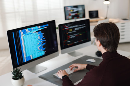 Programmer working on computer with dual monitors at white table in officeの写真素材