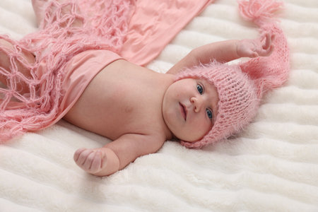 Cute newborn baby in pink hat and blanket lying on bedの写真素材