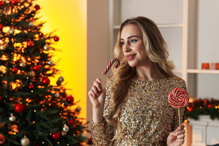 Woman with lollipop and candy cane in room decorated for Christmasの写真素材