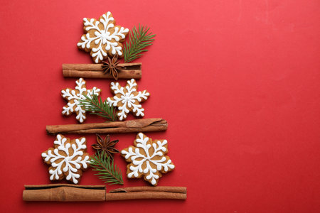 Christmas tree made of gingerbread cookies, cinnamon and fir branches on red background, flat lay.