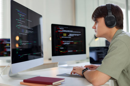 Programmer in headphones working on computer at white table in office