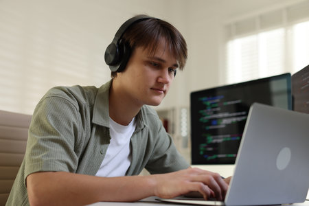 Programmer in headphones working on laptop at table in office, low angle viewの写真素材