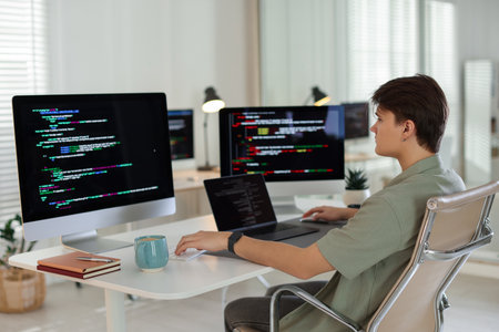 Programmer working on computer and laptop at white table in officeの写真素材