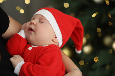 Cute newborn baby in Christmas costume and mother indoors, space for text. Bokeh effect