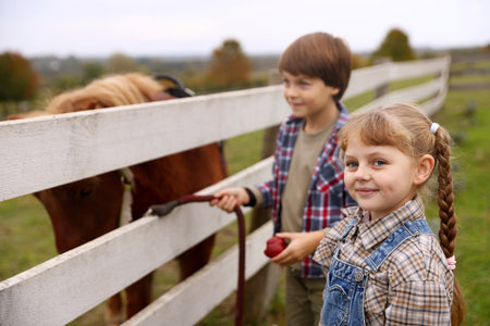 Equine assisted therapy. Cute children feeding apple to beautiful pony at paddock, selective focus. Lovely domesticated petの写真素材