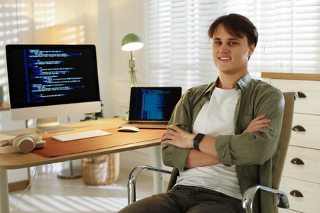 Portrait of smiling programmer with crossed arms on chair at workplaceの写真素材