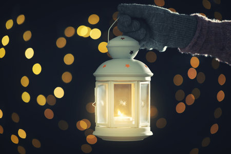 Merry Christmas and Happy Holidays. Woman holding lantern with candle against blurred lights on greeting cardの写真素材