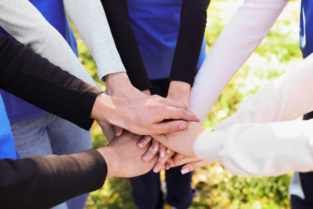 Group of volunteers stacking hands outdoors, closeup