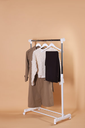 Different stylish clothes hanging on rack against beige backgroundの写真素材