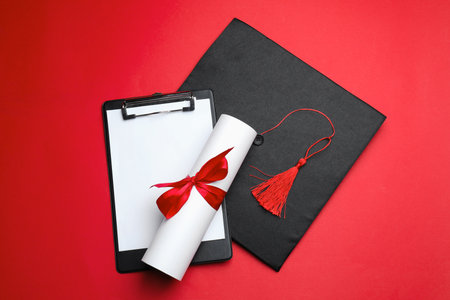 Diploma, graduation hat and clipboard on red background, flat lay