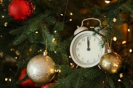 New Year greeting card. Alarm clock, festive lights and shiny baubles on fir tree branches, closeup....