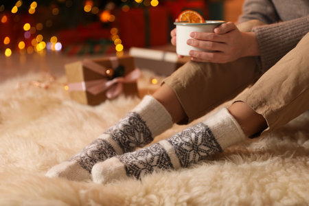 Woman in soft socks with delicious hot drink on floor against blurred Christmas lights, closeup. Bokeh effectの写真素材