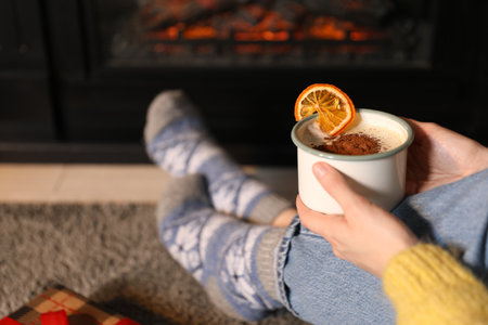 Woman wearing warm socks with delicious hot drink near fireplace at home, closeup. Cozy winter eveningの写真素材