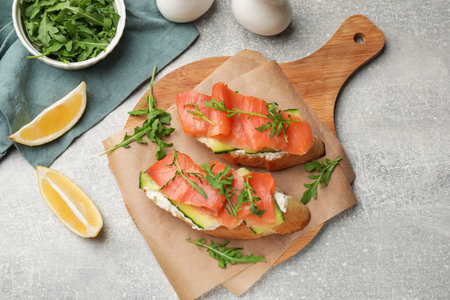 Tasty bruschettas with salmon, cream cheese, cucumber, arugula and lemon on gray table, flat layの写真素材