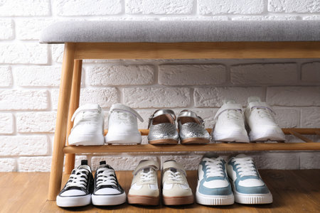 Different kid's shoes on storage bench near white brick wall indoorsの写真素材