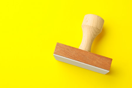 One wooden stamp on yellow background, top view. Space for textの写真素材