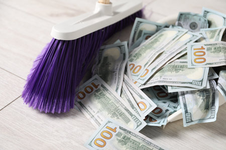 Sweeping dollar banknotes with broom into dustpan on light wooden floor, closeupの写真素材