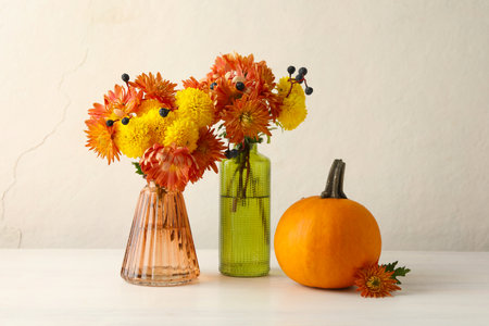 Autumn atmosphere. Vases with beautiful flowers, berries and pumpkin on white wooden tableの写真素材