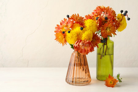 Autumn atmosphere. Vase with beautiful flowers and berries on white wooden table, space for textの写真素材