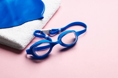 Swim cap, towel and goggles on pink background, closeup. Space for textの写真素材