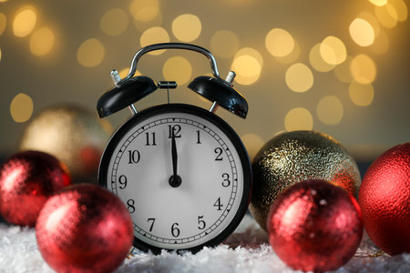 Alarm clock and shiny baubles on artificial snow against golden background with blurred lights, closeup. New Year greeting cardの写真素材