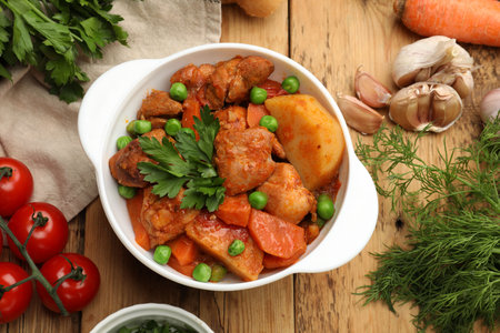 Delicious cooked stew in bowl and ingredients on wooden table, flat layの写真素材