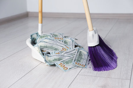Sweeping dollar banknotes with broom into dustpan on light wooden floor, closeupの写真素材