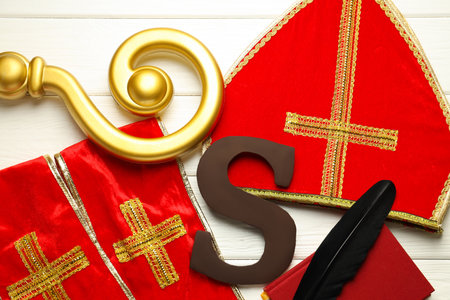 Sinterklaas (Saint Nicholas) Day. Chocolate letter S, mitre, stole, crosier and notebook with feather on white wooden background, flat layの写真素材