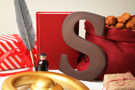 Sinterklaas (Saint Nicholas) Day. Chocolate letter S, sack with kruidnoten cookies, notebook with feather, gifts and crosier on white table, closeupの写真素材