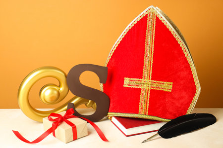 Sinterklaas (Saint Nicholas) Day. Chocolate letter S, mitre, crosier, gift, notebook and feather on white tableの写真素材
