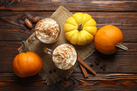 Tasty pumpkin latte with whipped cream in glass cups and ingredients on wooden table, flat layの写真素材
