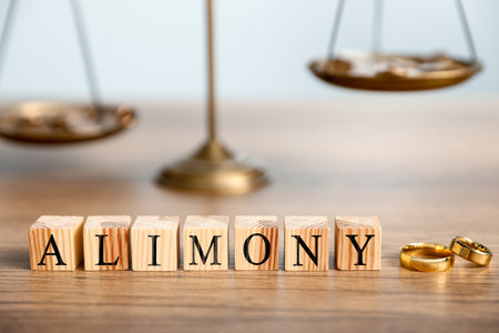 Alimony. Wedding rings, word made of cubes with letters and scale of justice on wooden tableの写真素材