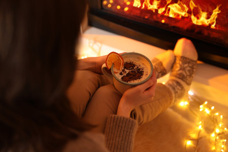 Woman with cup of cocoa sitting by fireplace at home, closeup. Christmas seasonの写真素材