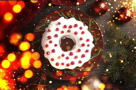 Tasty Christmas cake with red currants, fir branches and festive balls on wooden table, flat lay. Bokeh lightsの写真素材